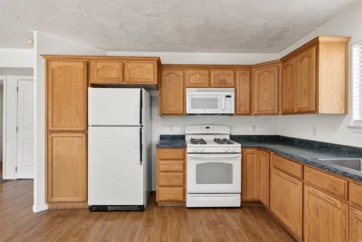 Kitchen featuring wood-finish cabinetry, dark countertops, white refrigerator, and a white oven with range