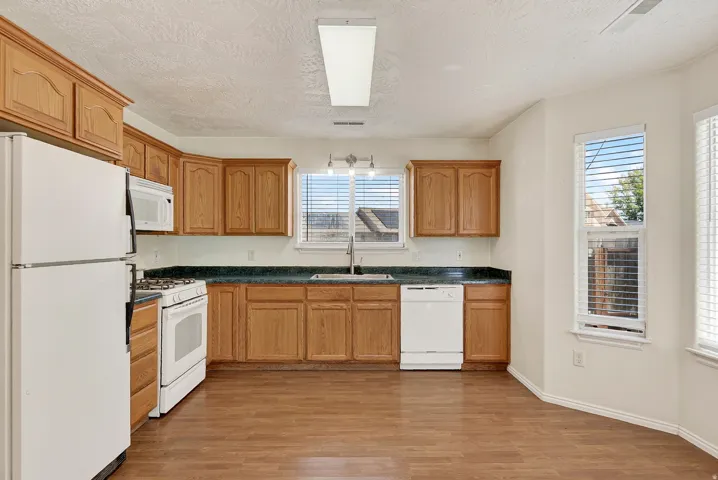 Kitchen featuring wood-finish flooring, oak cabinetry, dark countertops, and white appliances