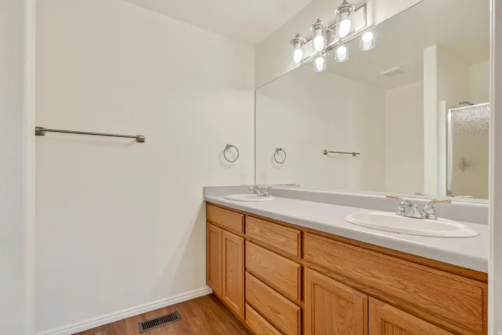 Dual vanity with wood-finish cabinetry, integrated sinks, and polished chrome fixtures
