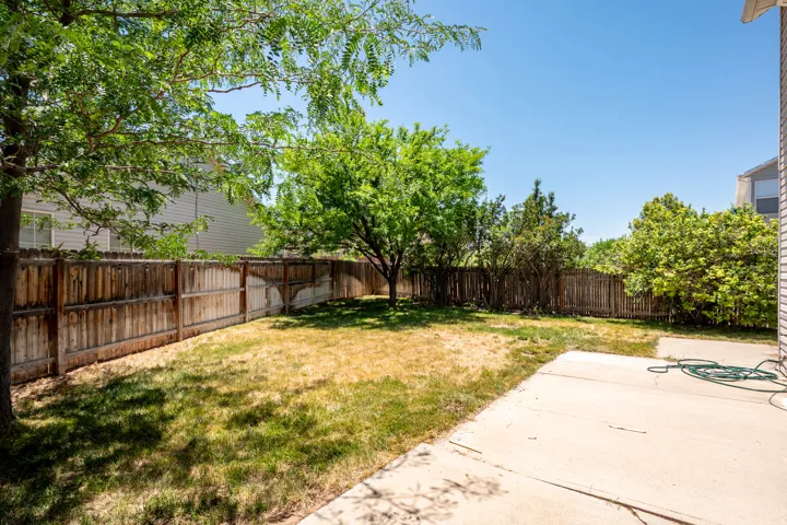 Expansive backyard featuring a concrete patio, wood fencing, and mature trees