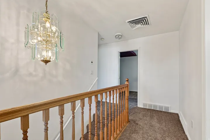Decorative chandelier, wood-finish stair railing, wall-to-wall carpeting, white painted walls, and white trim