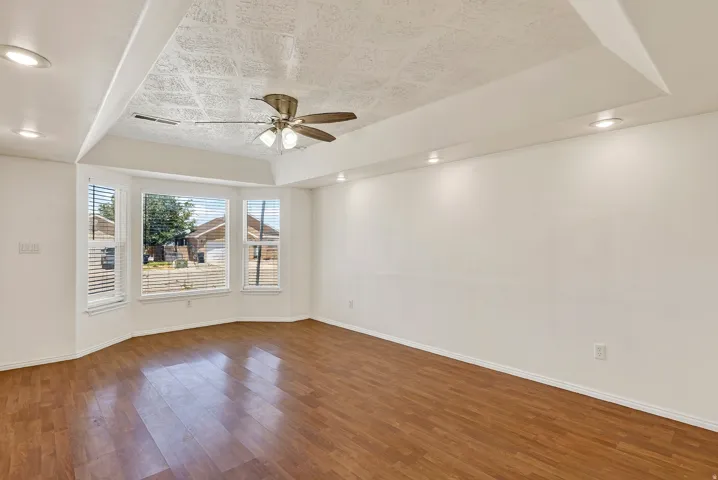 Recessed lighting illuminates the room, featuring wood-finish flooring and a tray ceiling