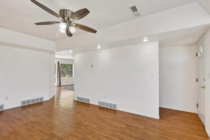 Wood-finish flooring, ceiling fan with integrated lighting, recessed lighting, white interior door with decorative glass, and a large window in the background