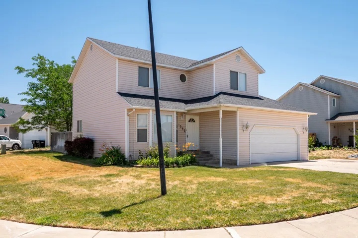 Two-story residence featuring light-colored siding, an attached garage, a covered front entry, and a paved driveway
