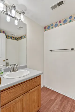Wood-finish flooring, wood cabinetry, built-in vanity with integrated sink, wall-mounted mirror, and brushed metal lighting fixture