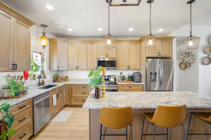 Kitchen featuring light wood cabinetry, stone countertops, stainless steel appliances, a center island with seating, and recessed lighting