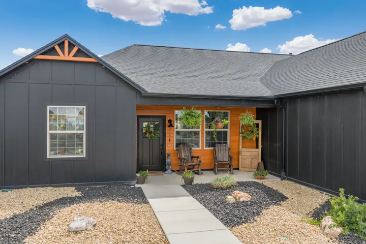 Board and batten siding, wood-paneled entry, asphalt shingle roof, concrete walkway, and gravel landscaping