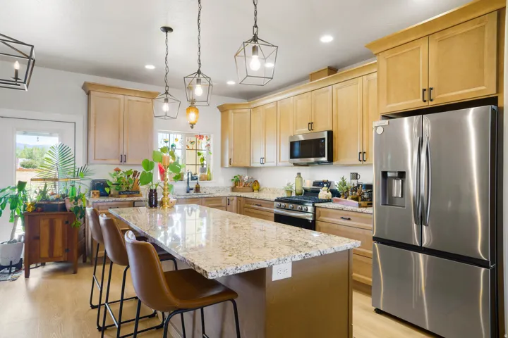 Kitchen featuring a spacious island with a light-toned countertop, wood-finish flooring, stainless steel appliances, and a collection of light wood-finish cabinetry