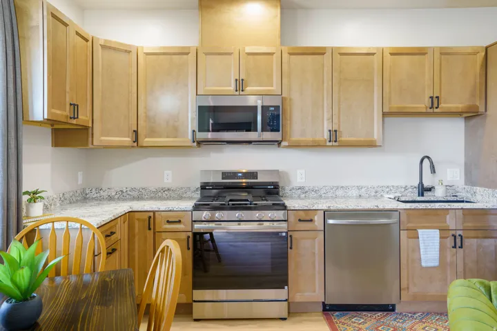 Kitchen featuring wood-finish cabinetry, stainless steel appliances, granite-style countertops, and a matte black gooseneck faucet