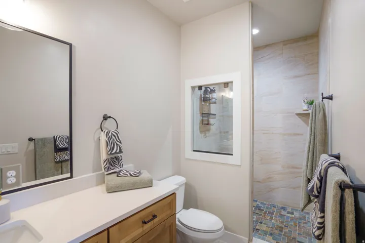 Walk-in shower with tiled walls and floor, wood-finish vanity with countertop, and framed mirror