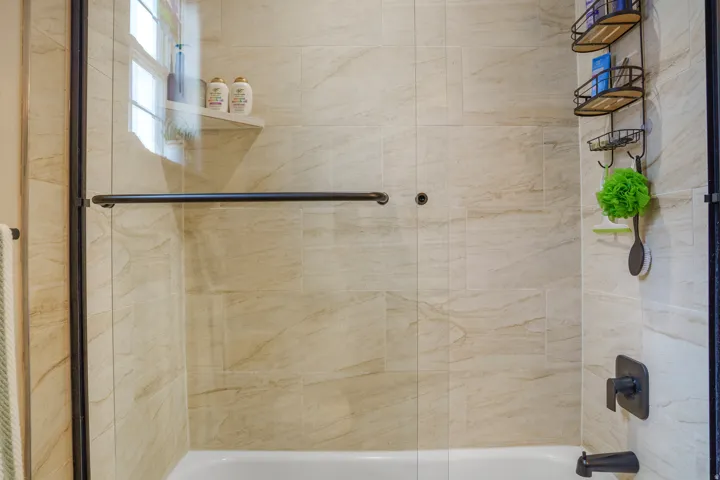 Built-in tub with glass enclosure, light-toned tile surround, and matte black fixtures