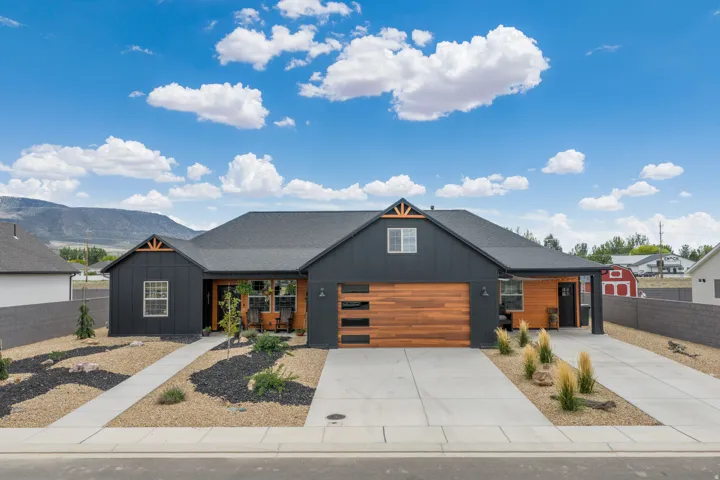 Contemporary exterior with dark siding, wood-finish garage door, prominent gables, and a wide driveway