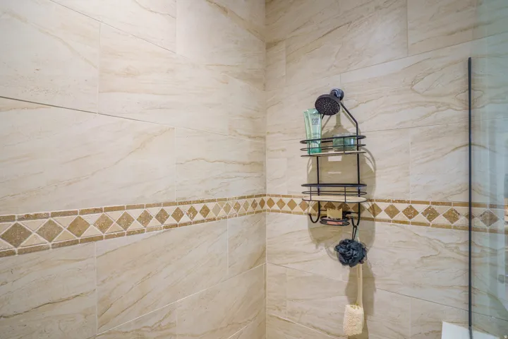 Textured tile shower surround with a decorative accent band and a dark-finish shower head