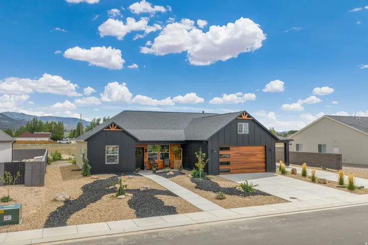Modern exterior with dark vertical siding, contrasting wood-tone garage door, and decorative gable truss