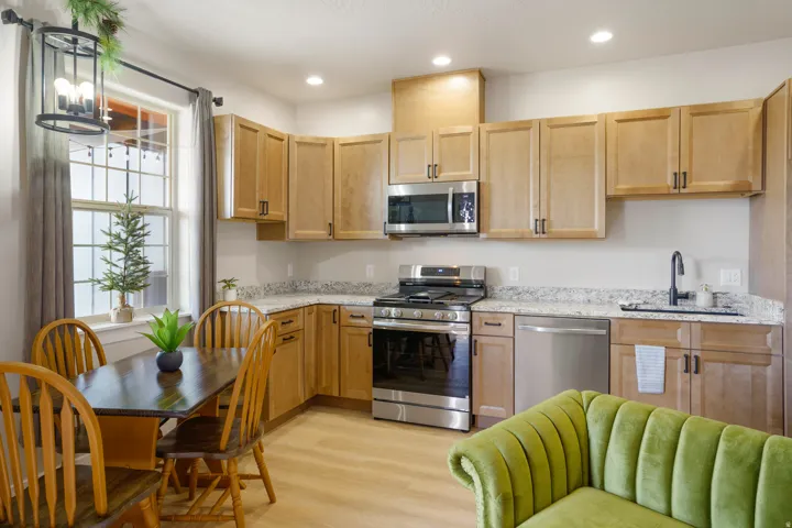 Light wood-finish cabinetry with black hardware, stainless steel appliances, speckled countertops, and wood-finish flooring