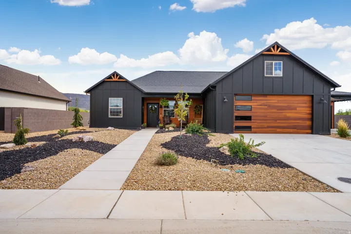 Modern farmhouse exterior with dark vertical siding, a wood-finish garage door, and decorative gable trusses
