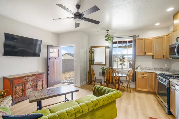 Open-concept living space featuring wood-finish flooring, a ceiling fan, and a kitchen with wood cabinetry, stainless steel appliances, and stone countertops