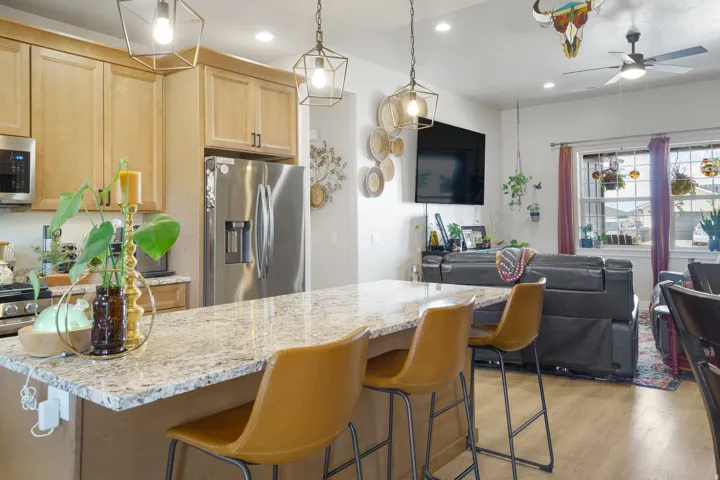 Kitchen island with a light-toned countertop, pendant lighting, stainless steel refrigerator, light wood-finish cabinetry, and wood-finish flooring
