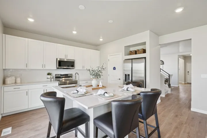 Kitchen featuring white shaker cabinetry, stainless steel appliances, a center island with countertop seating, and wood-finish flooring