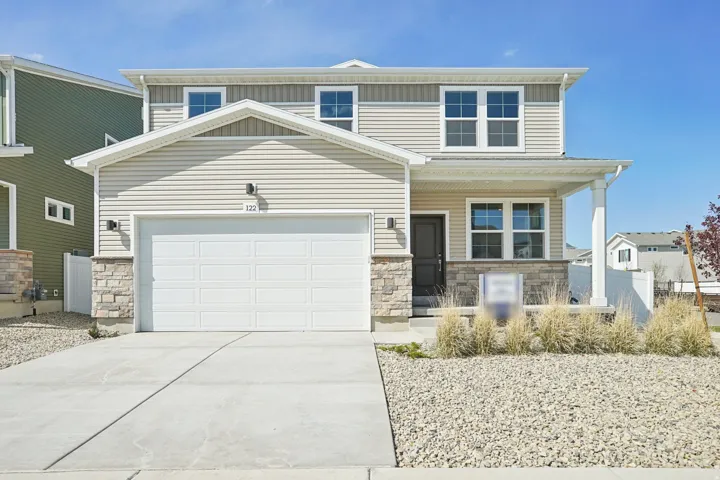 Two-story exterior with light-colored siding and stone accents, covered entry porch, attached garage, and concrete driveway