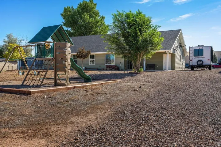 Rear exterior featuring green siding, a play structure with a slide, a covered porch, and a gravel surface