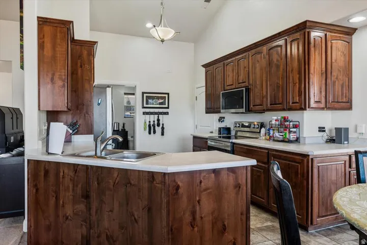 Kitchen featuring wood cabinetry, light-toned countertops, stainless steel appliances, and a vaulted ceiling