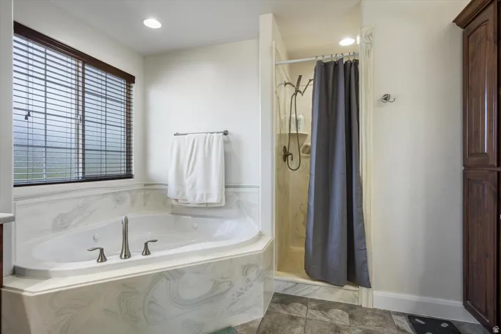 Soaking tub with brushed nickel fixtures, separate shower enclosure, wood-finish built-in cabinetry, and tile flooring