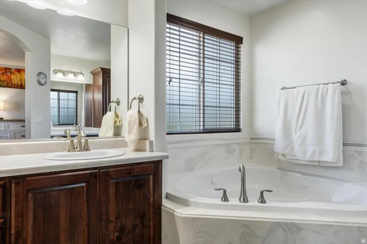 Built-in soaking tub with deck-mounted fixtures, wood-finish vanity with an undermount sink, and a framed mirror