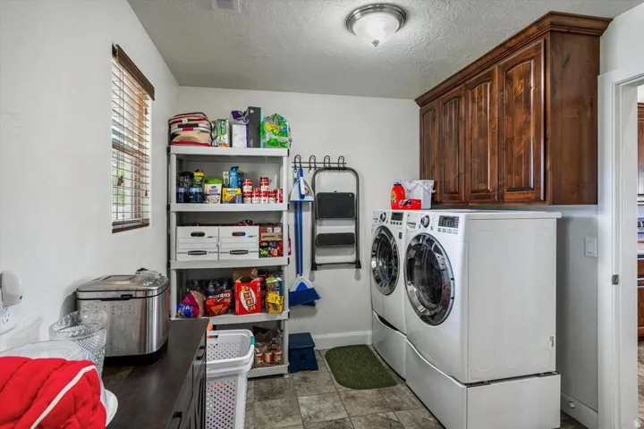 Dedicated laundry room featuring side-by-side front-load washers and dryers, abundant storage cabinetry with wood-finish doors, open shelving with organizational bins, stainless steel utility sink, and tile flooring throughout