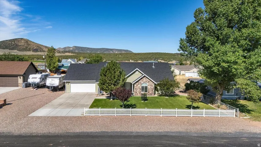 Single-story residence featuring a stone and siding exterior, an attached garage, a paved driveway, and a fenced front yard with a landscaped lawn