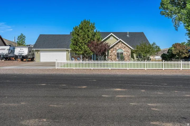 Exterior with light green siding, stone facade, a dark shingle roof, and a white picket fence