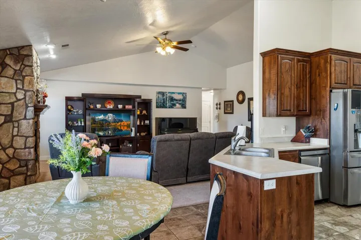 Vaulted ceiling with ceiling fan, stone-clad column, recessed lighting, wood-finish cabinetry, and stainless steel appliances