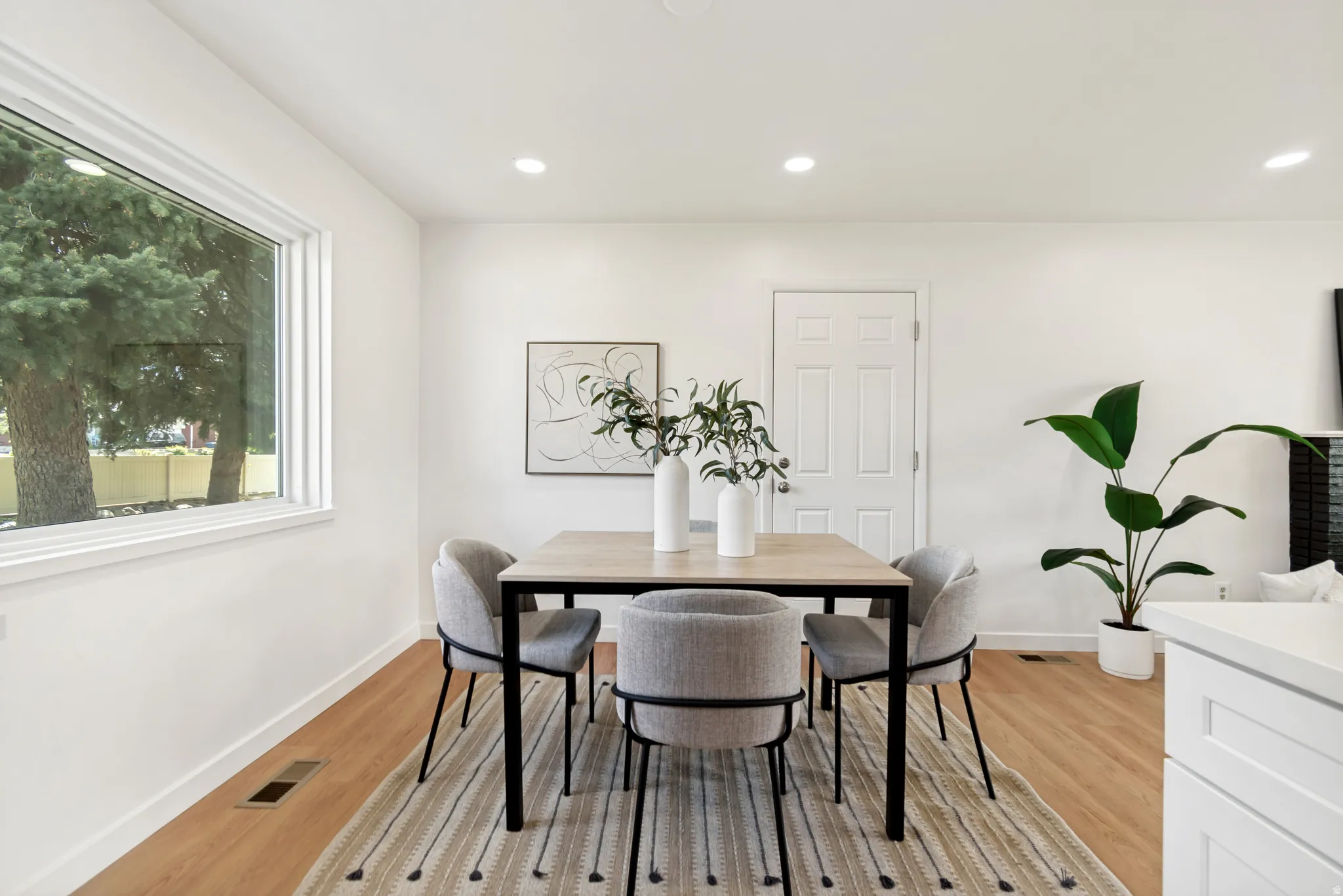 Expansive window, recessed ceiling lighting, light wood-finish flooring, white walls, and a white paneled door