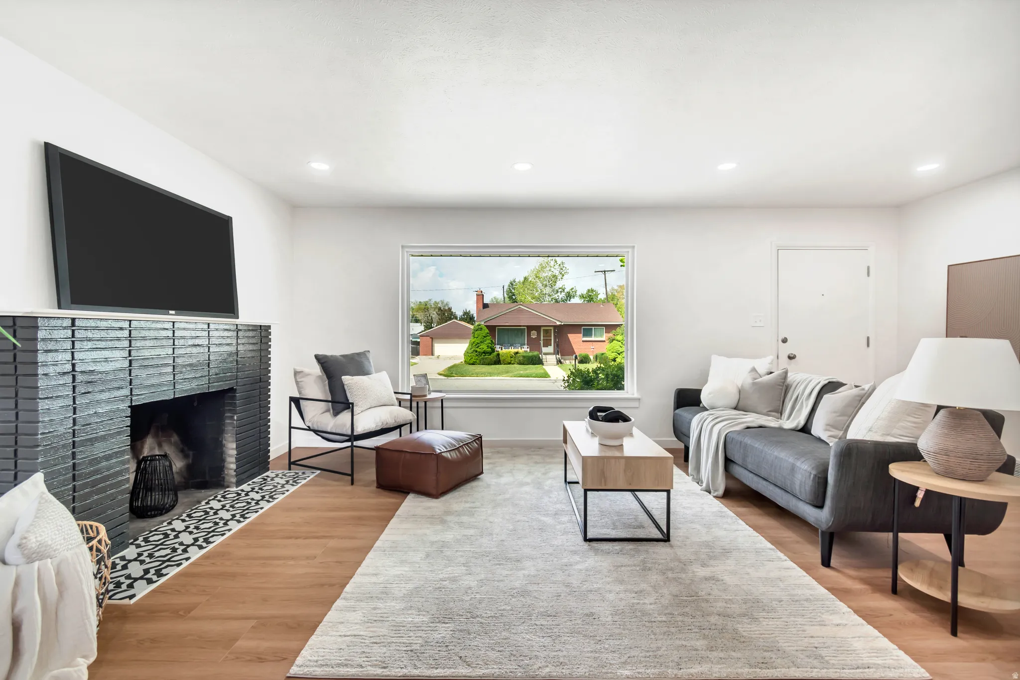 Spacious living area featuring wood-finish flooring, a modern black brick fireplace, recessed lighting, and a large picture window