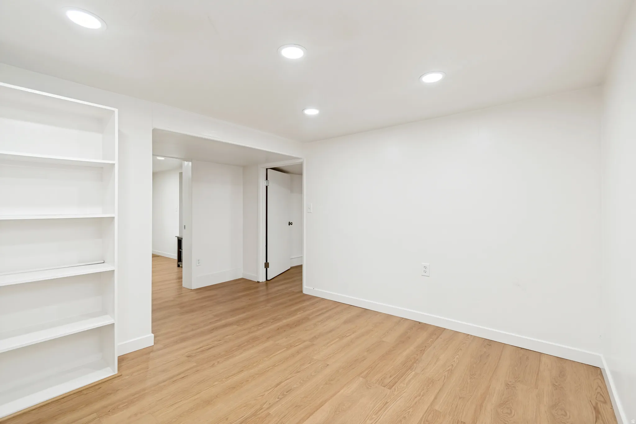 Recessed lighting, wood-finish flooring, white walls, built-in shelving, and white trim