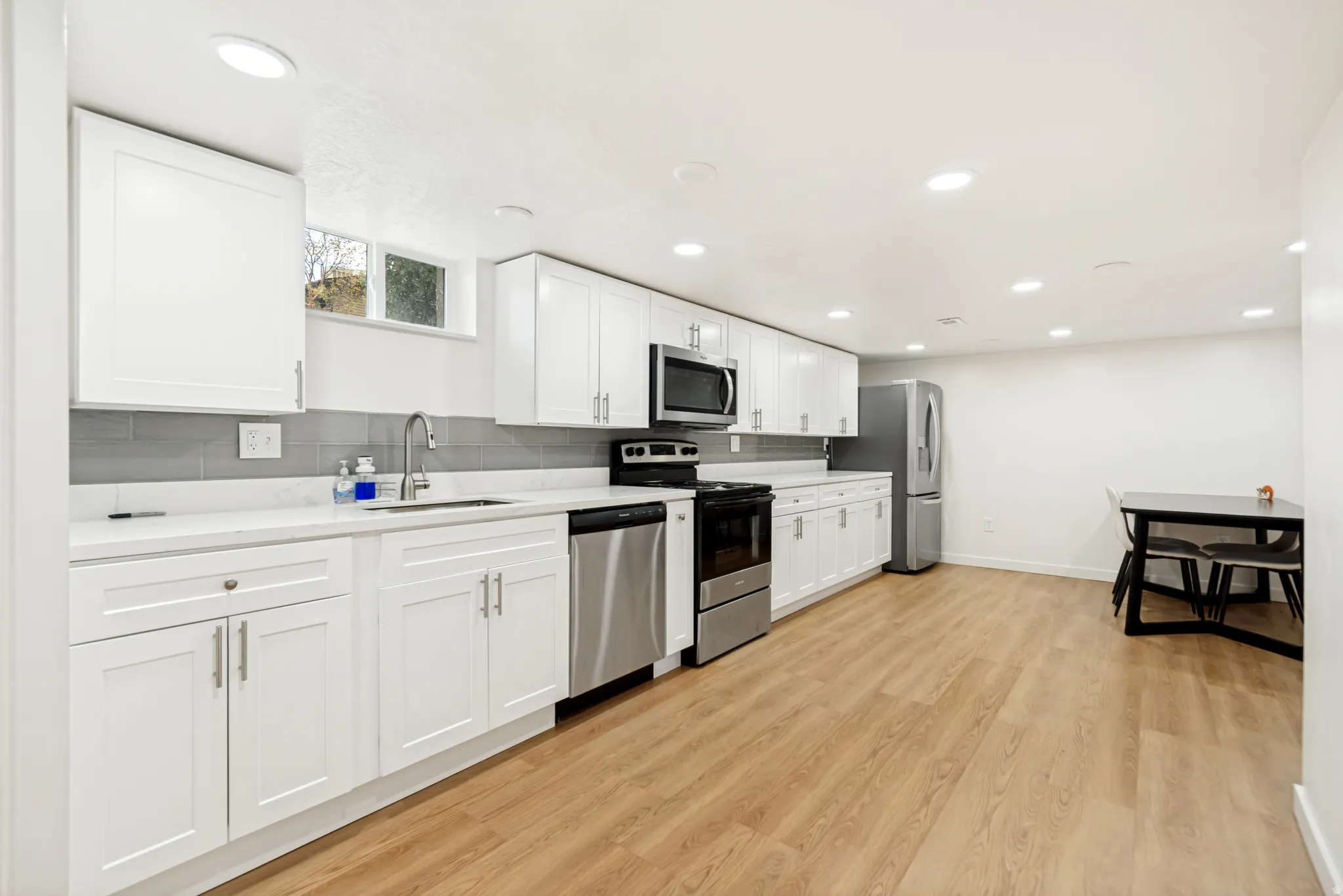 Kitchen featuring white shaker cabinetry, stainless steel appliances, a tile backsplash, light-toned wood-finish flooring, and recessed lighting