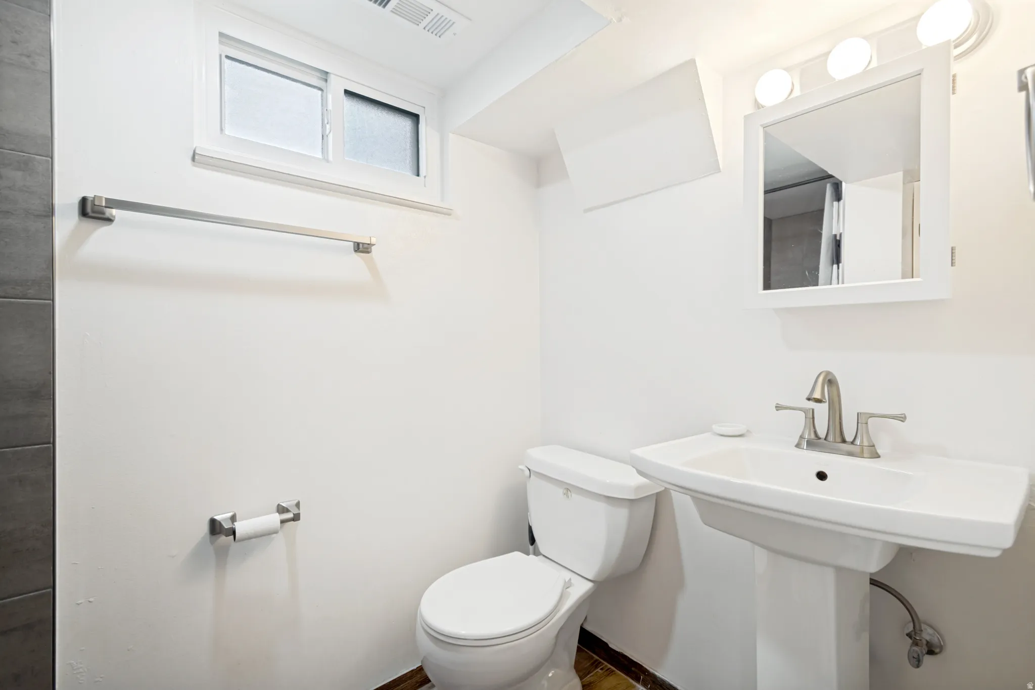 Pedestal sink with brushed nickel faucet, wall-mounted medicine cabinet with integrated lighting, and a window with privacy glass