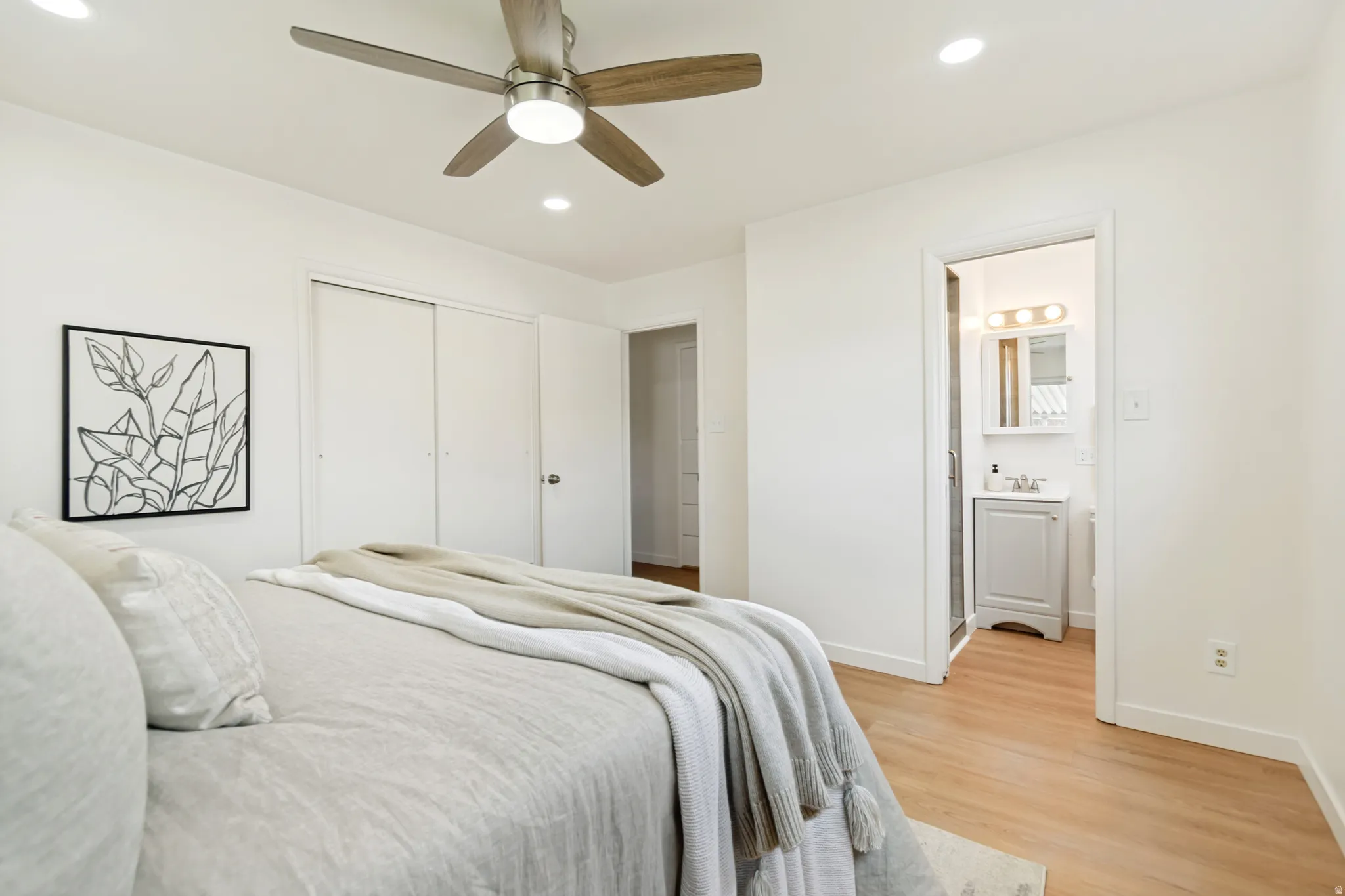 Recessed lighting, wood-finish flooring, ceiling fan with integrated light, sliding closet doors, and an attached bathroom with a vanity