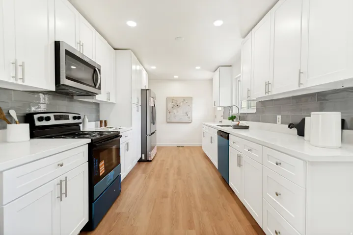 Galley kitchen featuring white cabinetry, light-toned wood-finish flooring, white countertops, and a gray tile backsplash