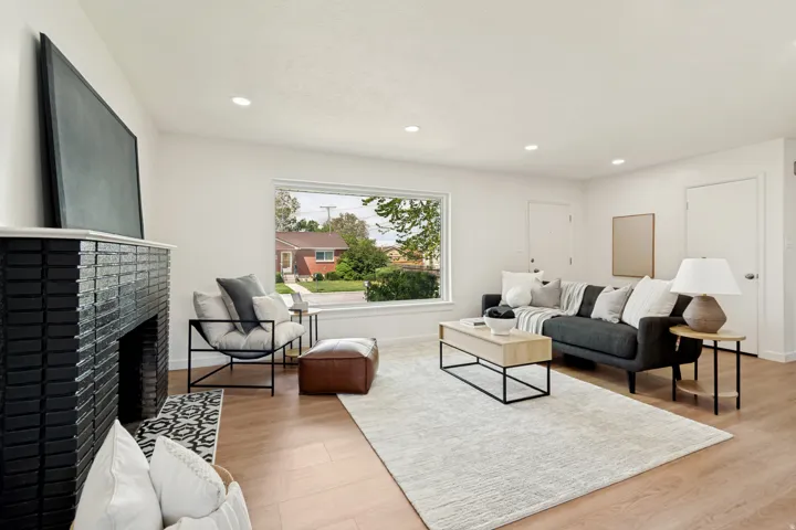 Spacious living area featuring a fireplace with a black tile surround and a white mantel, a large picture window, recessed lighting, and wood-finish flooring