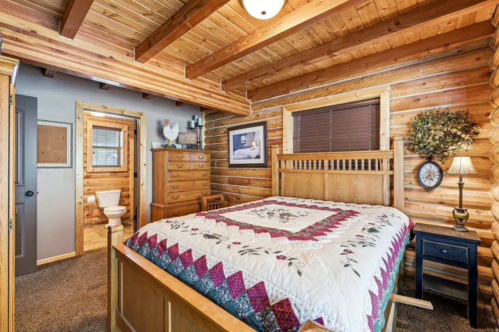 Exposed log walls, natural wood plank ceiling with exposed beams, wood-frame window with blinds, wood cabinetry, and wood-finish door