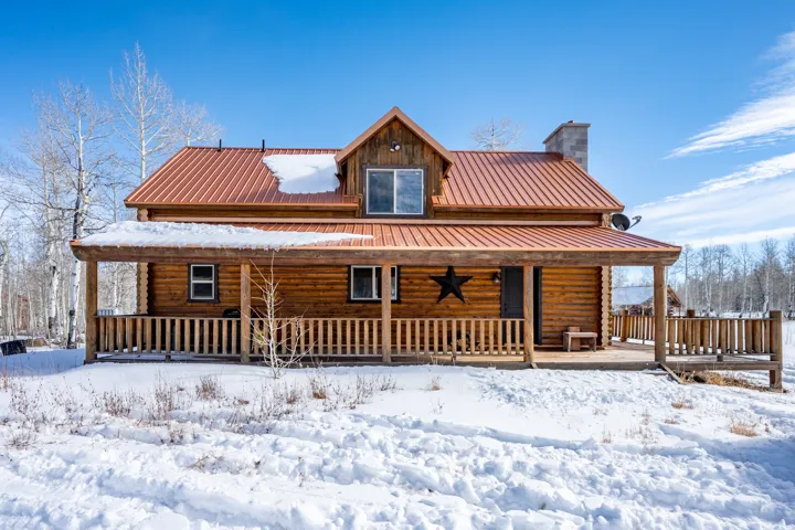 Log cabin exterior with a copper-toned metal roof, a full-width covered porch, and a stone chimney