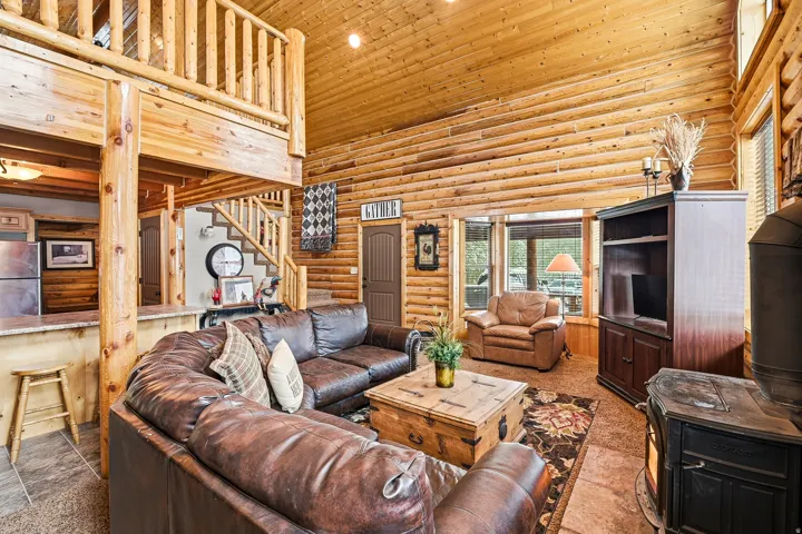 Vaulted wood-paneled ceiling, exposed log beams, wood stove, built-in display cabinetry, and a wood staircase with an open railing