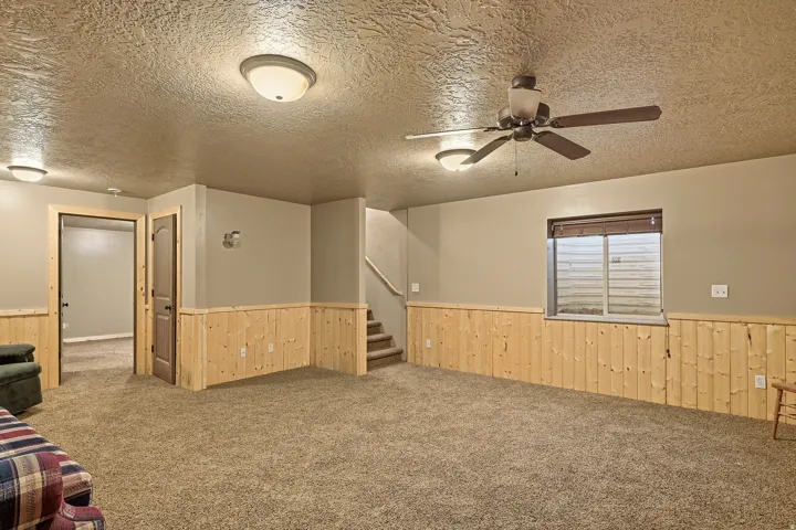 Carpeted room featuring wood panel wainscoting and a ceiling fan