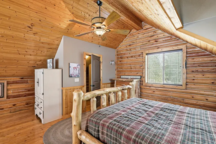 Vaulted wood plank ceiling, wood plank walls, wood-finish flooring, built-in ceiling fan with light fixture, and window with blinds