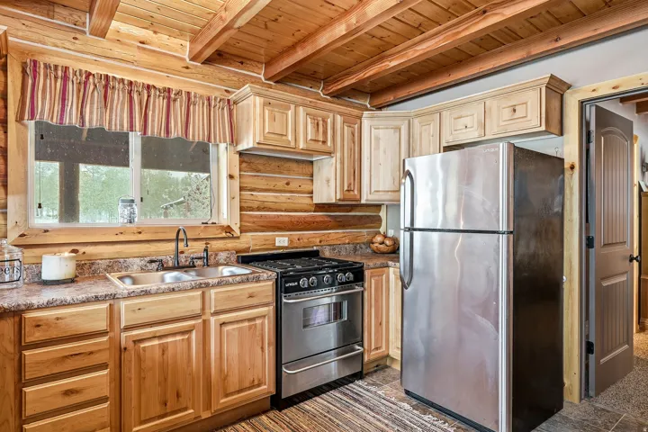 Wood-paneled ceiling with exposed beams, wood-finish cabinetry, stainless steel appliances, and a double basin sink