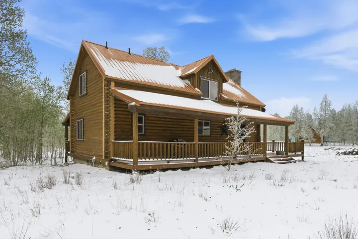 Log cabin exterior featuring a covered porch, an upper-level dormer, a metal roof, and a visible chimney