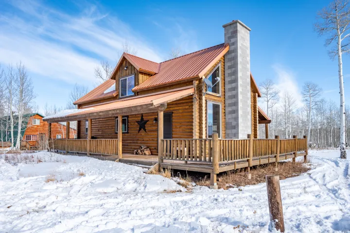Log exterior with a red metal roof, full-length covered front porch, an expansive wood deck, and a prominent stone chimney