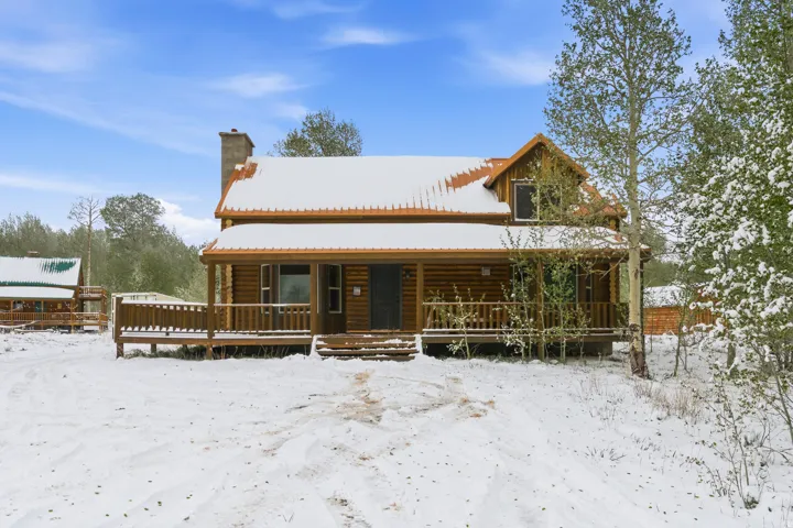 Log cabin exterior featuring a covered porch, wood siding, and an exposed stone chimney