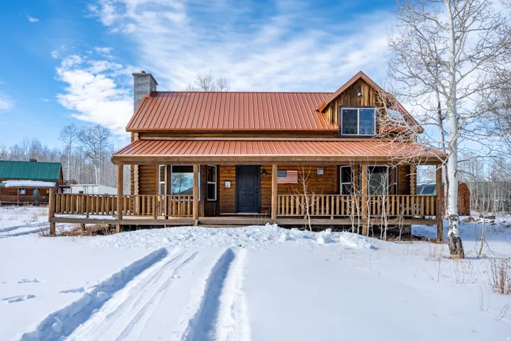 Log cabin exterior with a metal roof and a covered front porch featuring a wood railing
